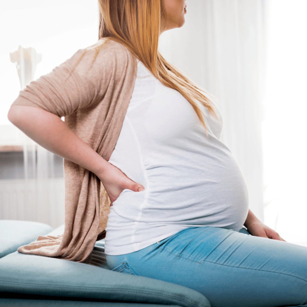 alt="pregnant woman sitting on bed holding her back in pain"